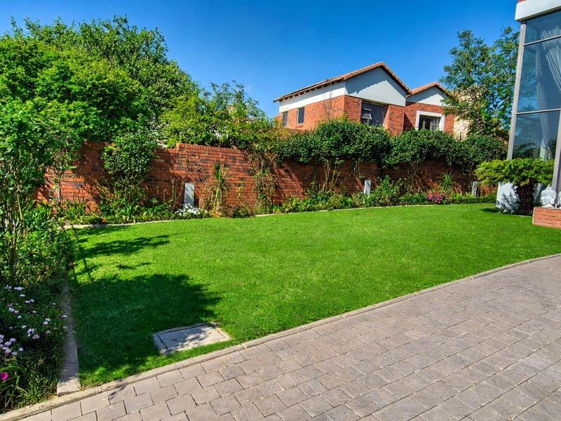 A well-maintained rear garden featuring a manicured lawn, paved patio area, and a brick boundary wall, providing a private outdoor space.
