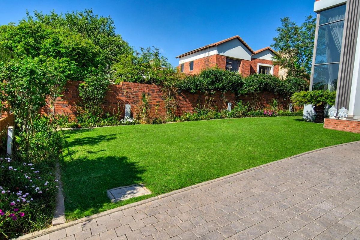 A well-maintained rear garden featuring a manicured lawn, paved patio area, and a brick boundary wall, providing a private outdoor space.