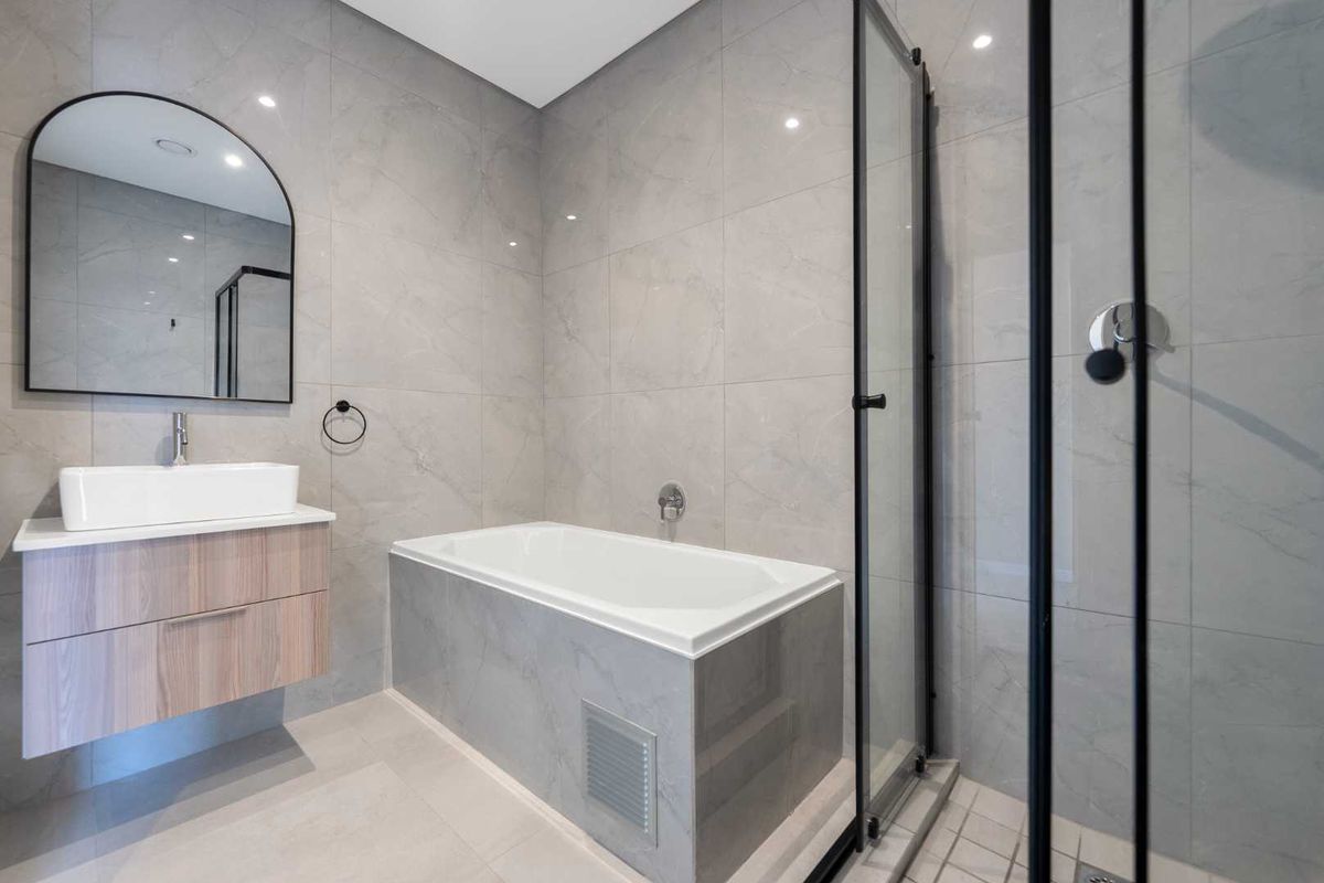 Modern bathroom featuring a wall-mounted vanity, vessel sink, built-in bathtub, and a separate glass-enclosed shower with neutral grey tiling throughout.