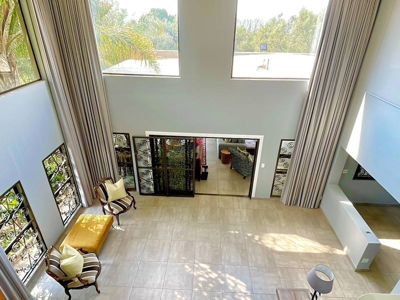 Spacious double-volume living area featuring expansive windows, tiled flooring, and an open-plan design with a mezzanine overlook.