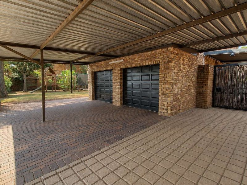 A well-maintained double garage with a spacious attached carport, featuring brick exterior walls and paved driveway area.