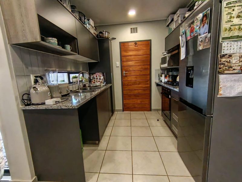 A functional galley-style kitchen featuring modern dark cabinetry, granite countertops, tiled flooring, and a solid timber door.