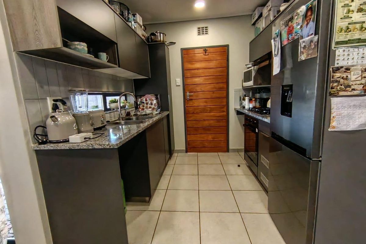 A functional galley-style kitchen featuring modern dark cabinetry, granite countertops, tiled flooring, and a solid timber door.