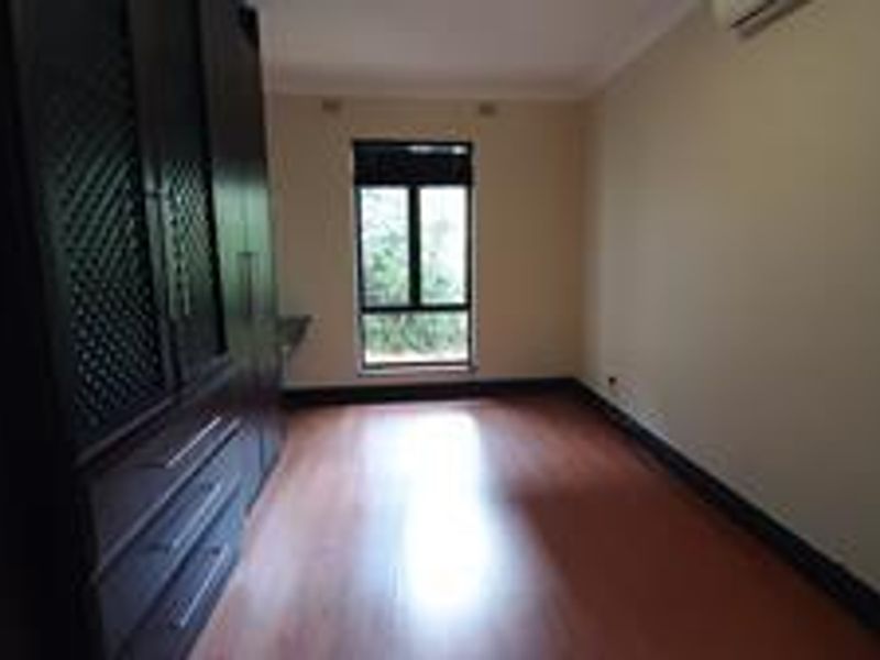 A spacious bedroom featuring laminate flooring, built-in cupboards, and an integrated air conditioning unit.