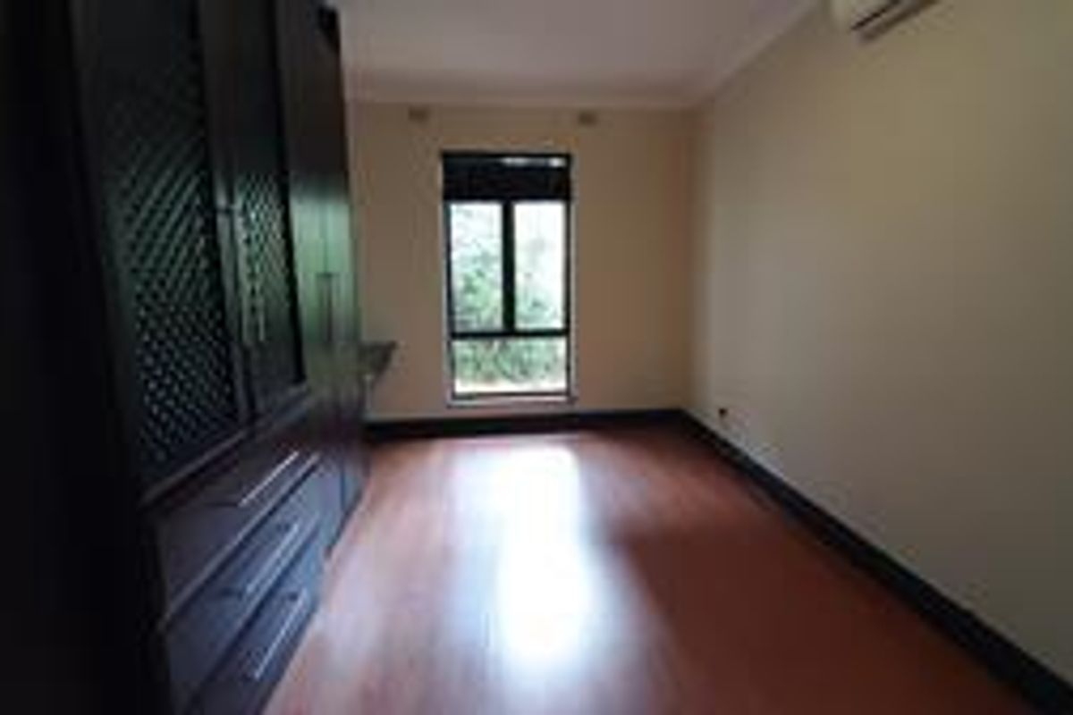 A spacious bedroom featuring laminate flooring, built-in cupboards, and an integrated air conditioning unit.