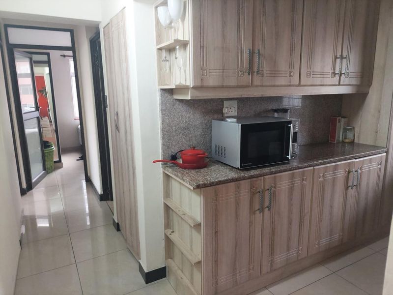 A functional kitchen area featuring wood-look laminated cabinetry, granite countertops, and tiled flooring, with an adjacent hallway leading to other rooms.