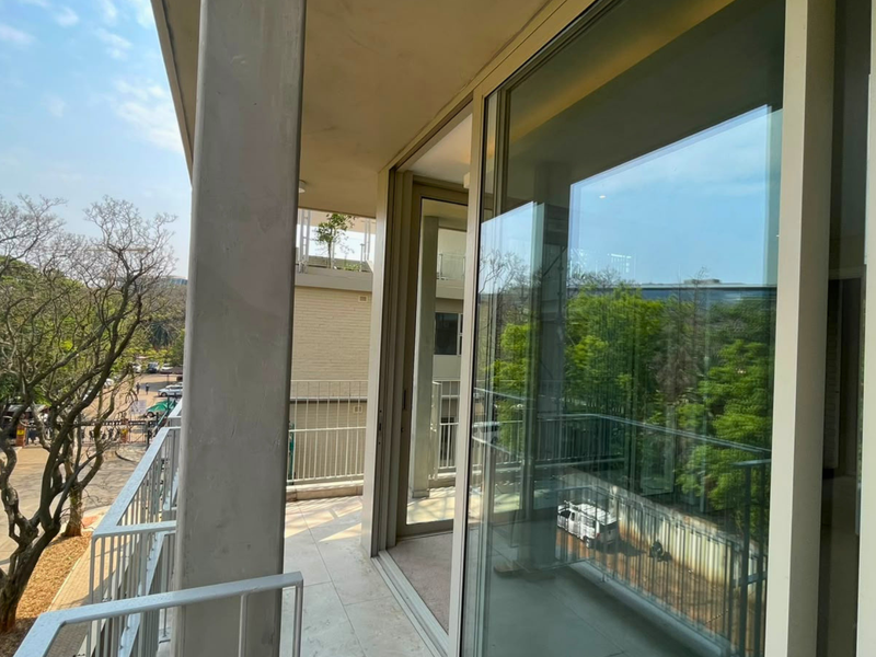 A spacious apartment balcony featuring tiled flooring, a metal balustrade, and large sliding glass doors providing access to the interior living space.