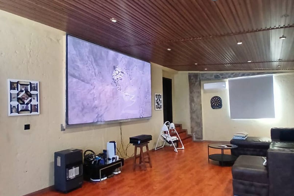 Spacious living area featuring warm-toned laminate flooring, a distinctive timber-slat ceiling with recessed lighting, and a wall-mounted air conditioning unit.