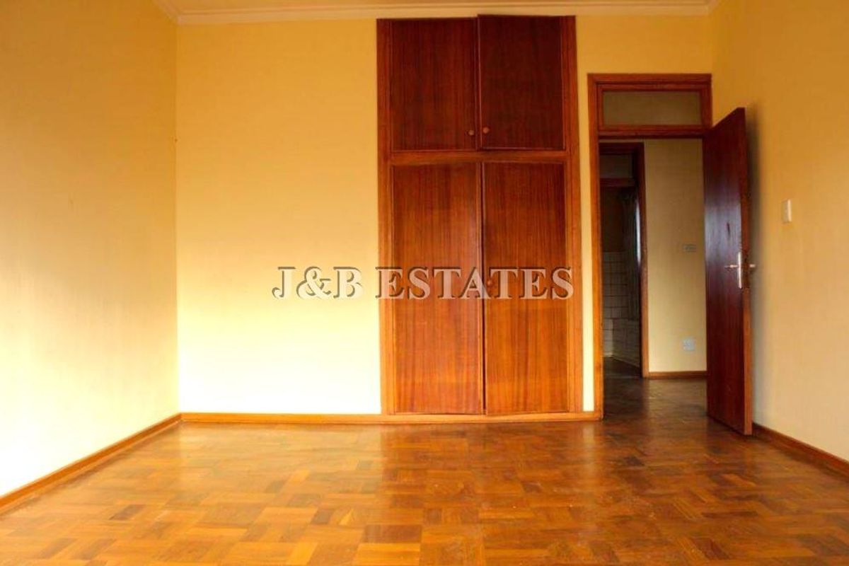A bedroom featuring built-in wooden cupboards and traditional parquet flooring, with an open doorway leading to an adjacent room.