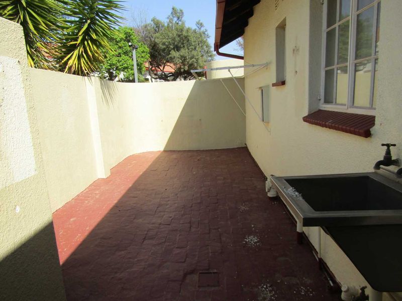 A functional outdoor utility area featuring a stainless steel sink, brick paving, and a wall-mounted drying rack, suitable for laundry or general maintenance tasks.