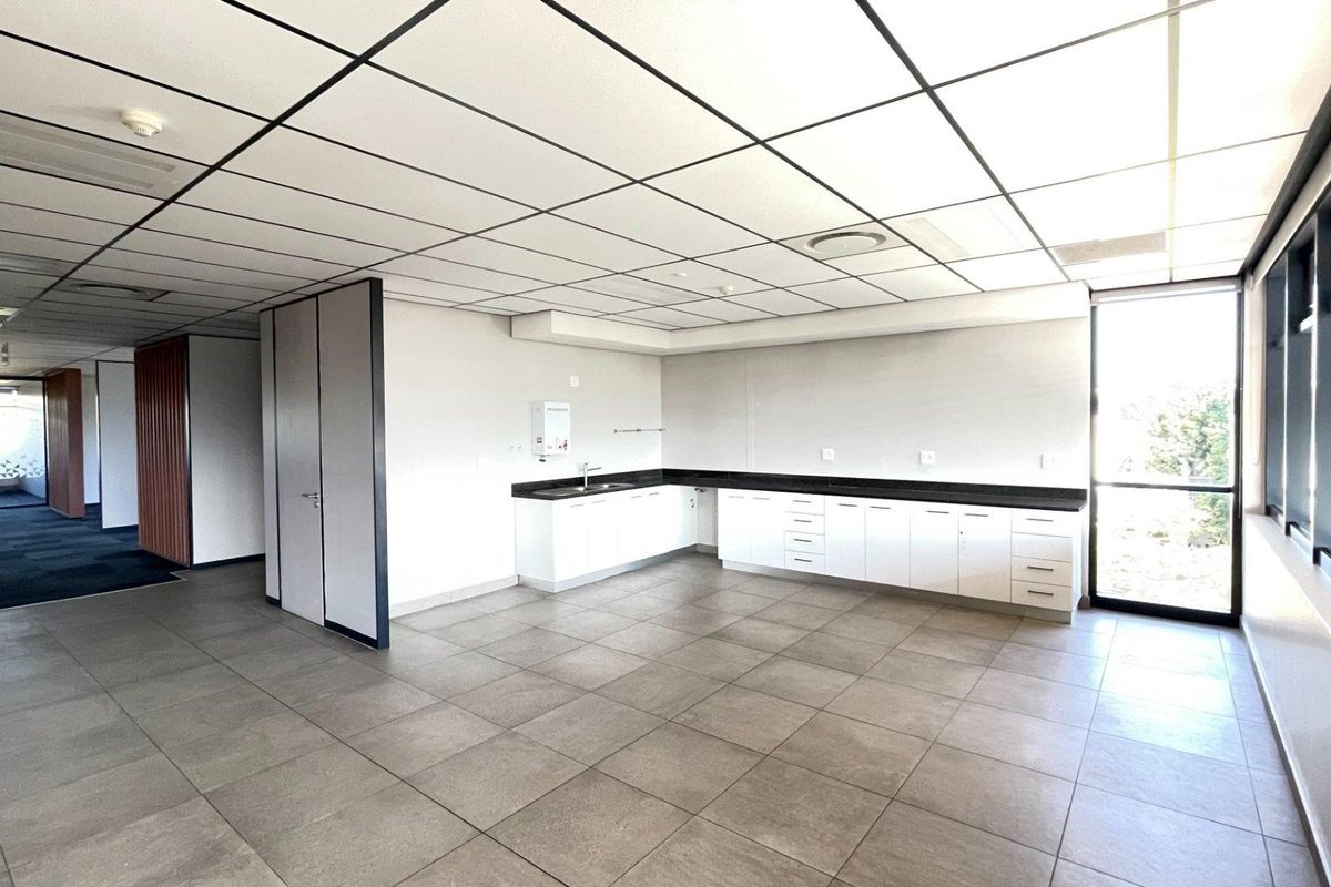 A clean, modern office kitchenette featuring white cabinetry, dark countertops, tiled flooring, and a drop ceiling, offering a functional space for staff.