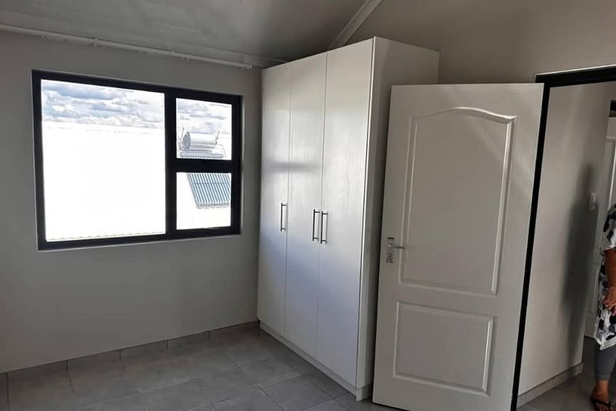 A bright bedroom featuring built-in white cabinetry, tiled flooring, and a large window providing natural light.