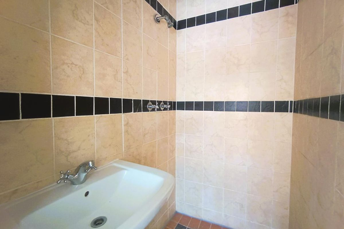 A functional bathroom featuring a wall-mounted basin and a tiled shower enclosure with a classic beige and black decorative border.