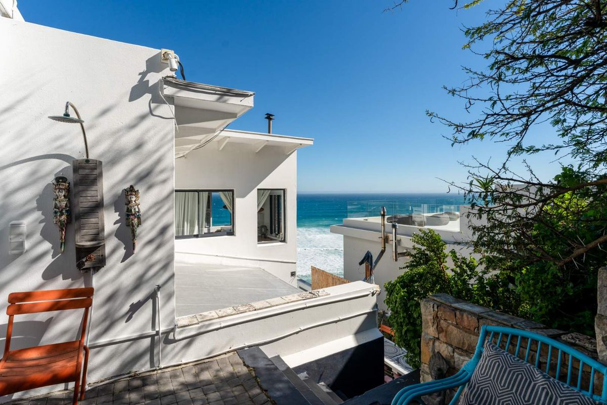 Rear exterior view featuring a paved terrace, outdoor shower, and glass balustrade overlooking the ocean.
