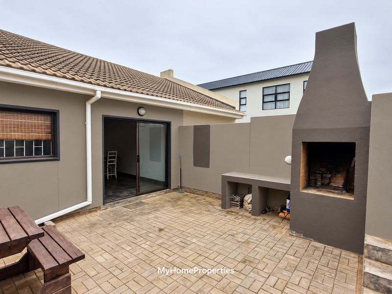 A private paved patio area featuring a built-in braai, concrete prep counter, and direct access to the interior through a sliding door.