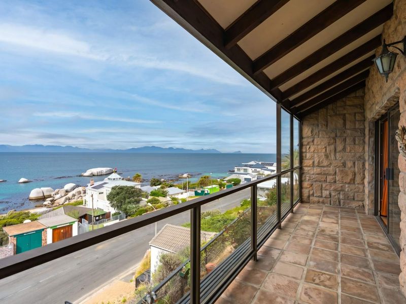 A spacious covered balcony featuring stone wall cladding, exposed timber beams, and a glass balustrade, offering expansive coastal and ocean views.