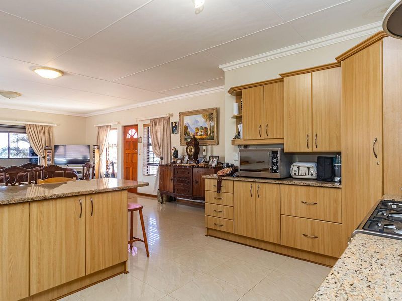 Open-plan kitchen and living area featuring light wood cabinetry, granite countertops, gas hob, and neutral tiled flooring throughout the space.