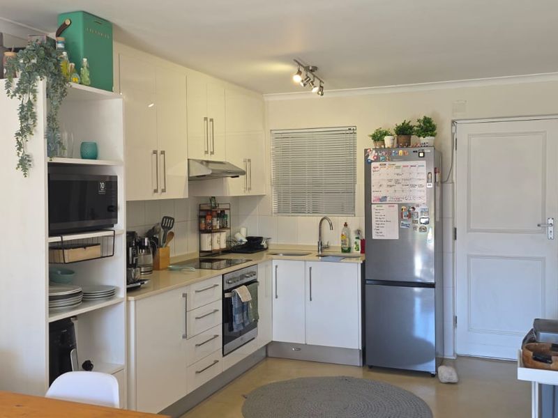 A functional kitchen featuring white gloss cabinetry, a tiled backsplash, built-in oven with extractor fan, and a stainless steel sink.