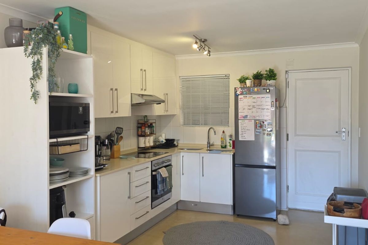 A functional kitchen featuring white gloss cabinetry, a tiled backsplash, built-in oven with extractor fan, and a stainless steel sink.