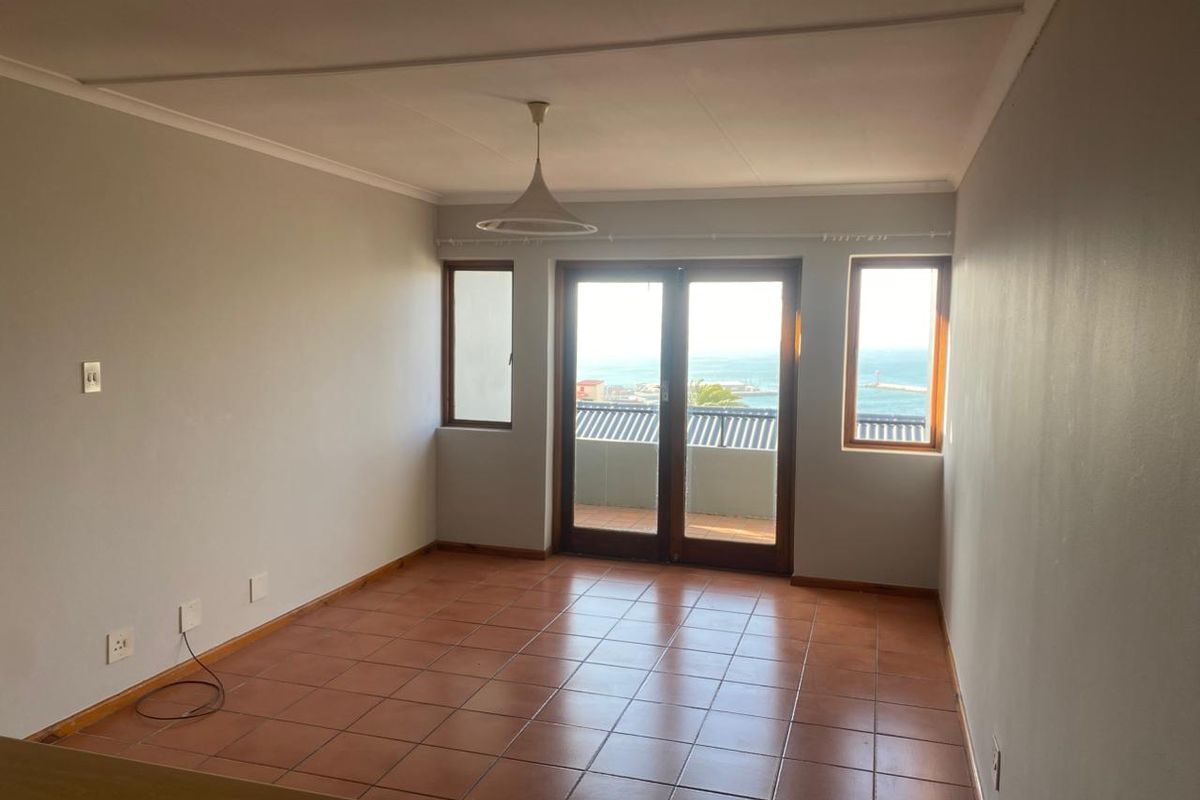 An empty living room featuring tiled flooring, a pendant light, and double glass doors opening to a balcony with ocean views.