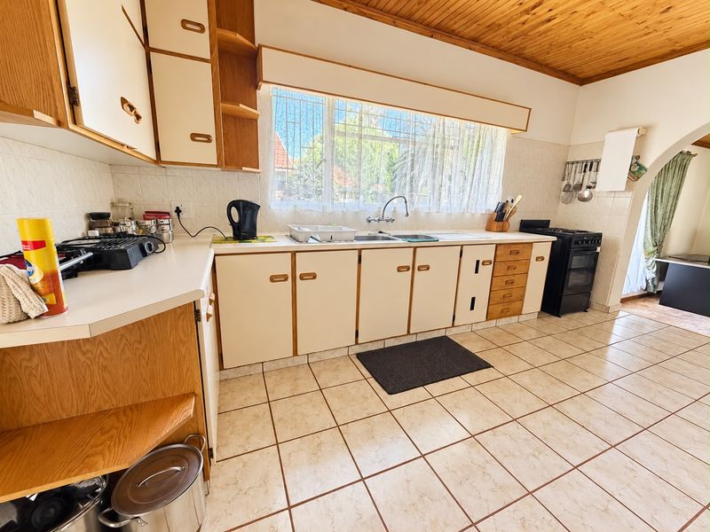 A functional kitchen featuring dated laminate cabinetry, tiled flooring, a timber ceiling, and a tiled backsplash with a window overlooking the exterior.