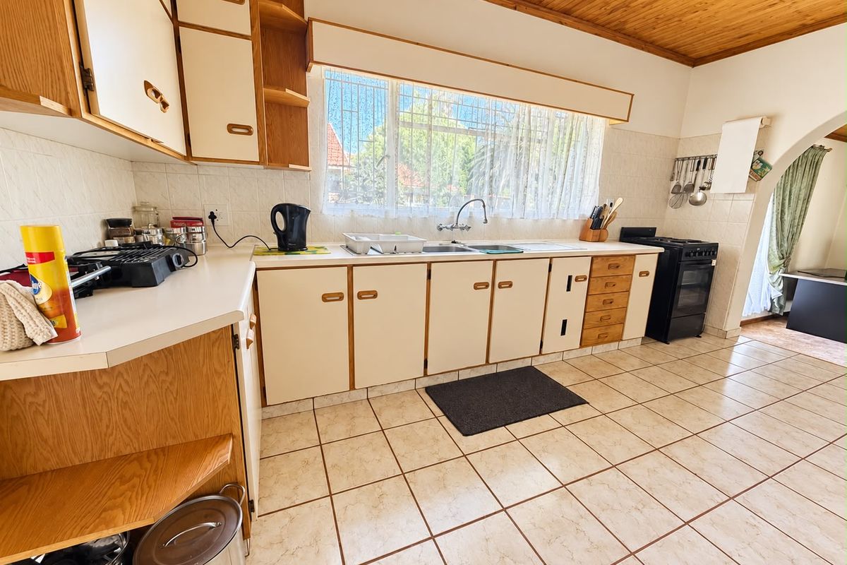 A functional kitchen featuring dated laminate cabinetry, tiled flooring, a timber ceiling, and a tiled backsplash with a window overlooking the exterior.