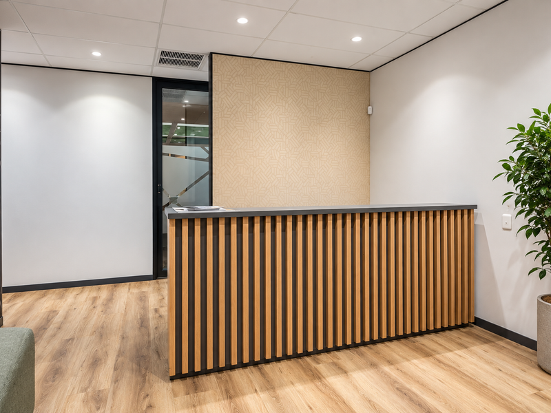 Modern office reception area featuring a slatted timber-fronted desk, wood-look flooring, and professional recessed lighting.