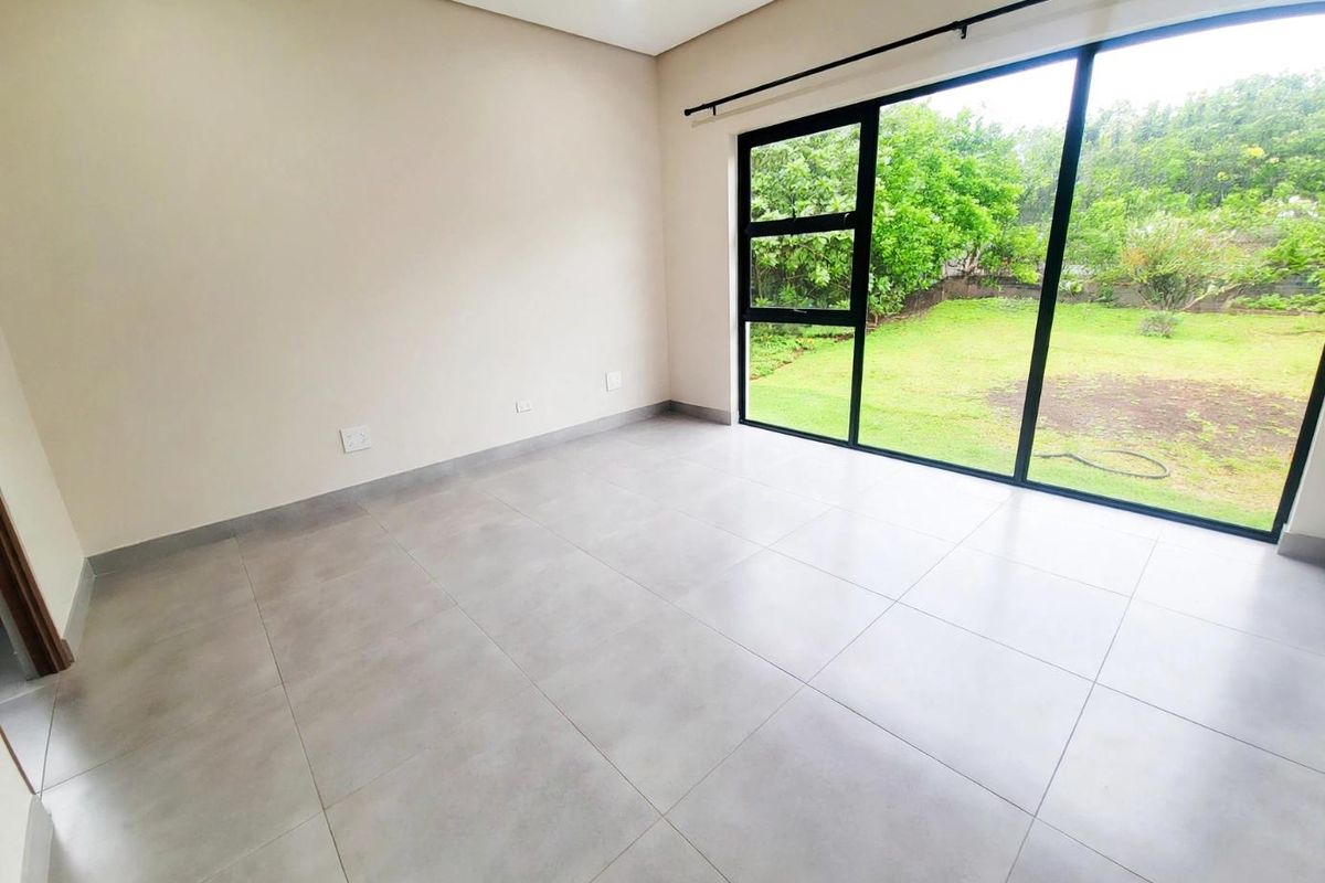 A bright, modern, and empty bedroom featuring large-format floor tiles, recessed lighting, and expansive black aluminium sliding doors opening to a garden view.
