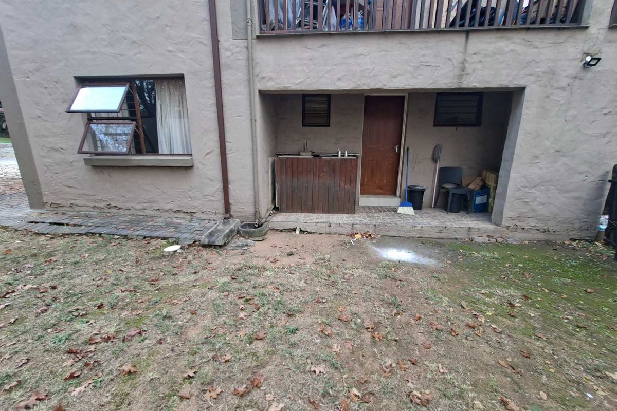 Rear view of the apartment building featuring a covered patio area, tiled flooring, and access to a small private garden space.