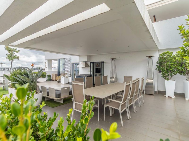 Spacious covered penthouse balcony featuring a built-in braai, tiled flooring, and recessed lighting, ideal for outdoor dining and entertaining.