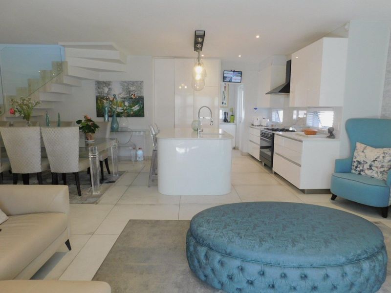 Modern open-plan living area featuring a sleek white kitchen with a central island, gas hob, and integrated cabinetry, complemented by tiled floors and a staircase.