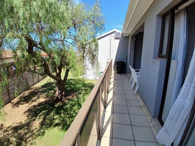 A tiled balcony featuring a glass and metal balustrade, overlooking a private garden area with mature trees.