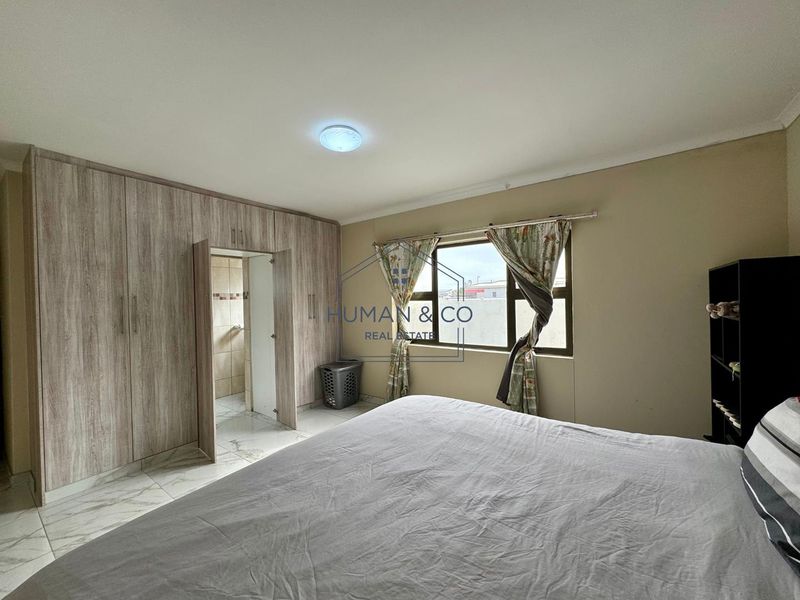 A bedroom featuring built-in cupboards, tiled flooring, and an en-suite bathroom entrance, offering a functional layout with natural light.