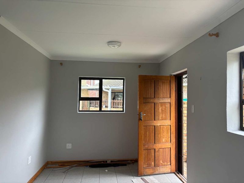 A clean, empty bedroom featuring neutral grey walls, tiled flooring, and a solid timber door, ready for personalization.