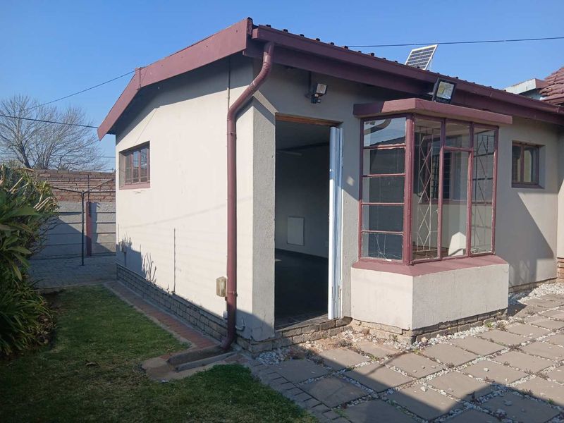 Rear view of the cottage featuring a bay window, solar panel, and paved patio area with access to the interior.