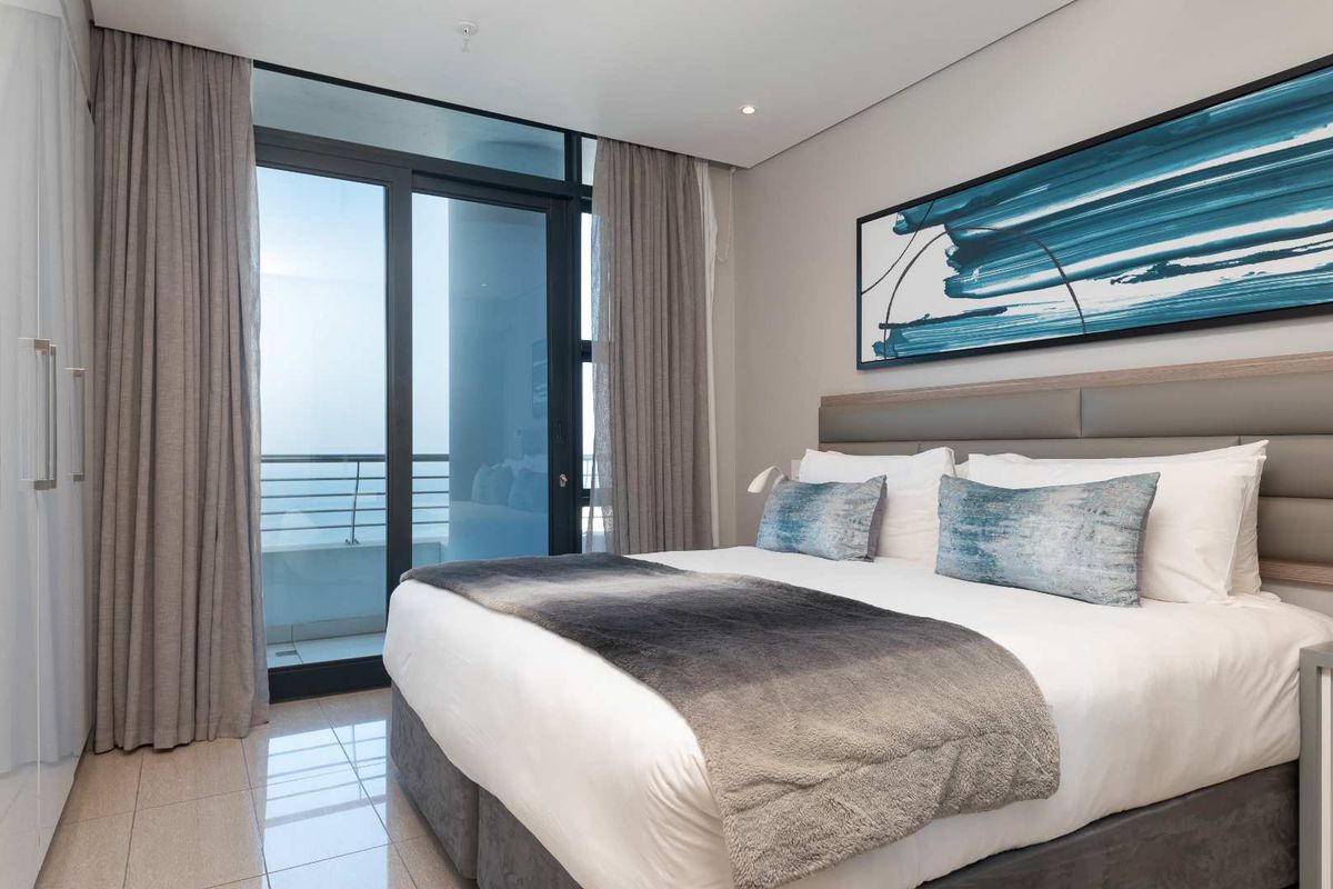 A modern, well-maintained bedroom featuring tiled flooring, a built-in upholstered headboard, and a large sliding glass door providing access to a private balcony.
