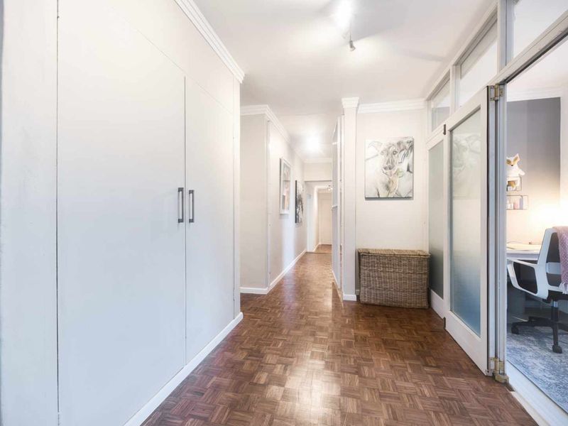A bright, well-maintained hallway featuring classic parquet flooring, extensive built-in storage cupboards, and glass-panelled doors leading to adjacent rooms.
