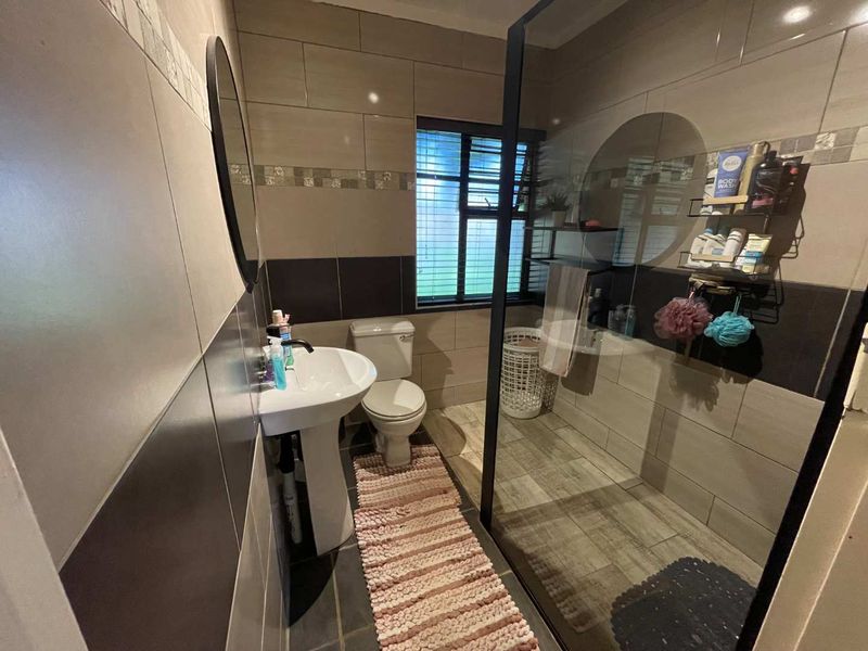 Modern bathroom featuring a walk-in shower with a black-framed glass screen, pedestal basin, toilet, and contemporary tiled finishes.