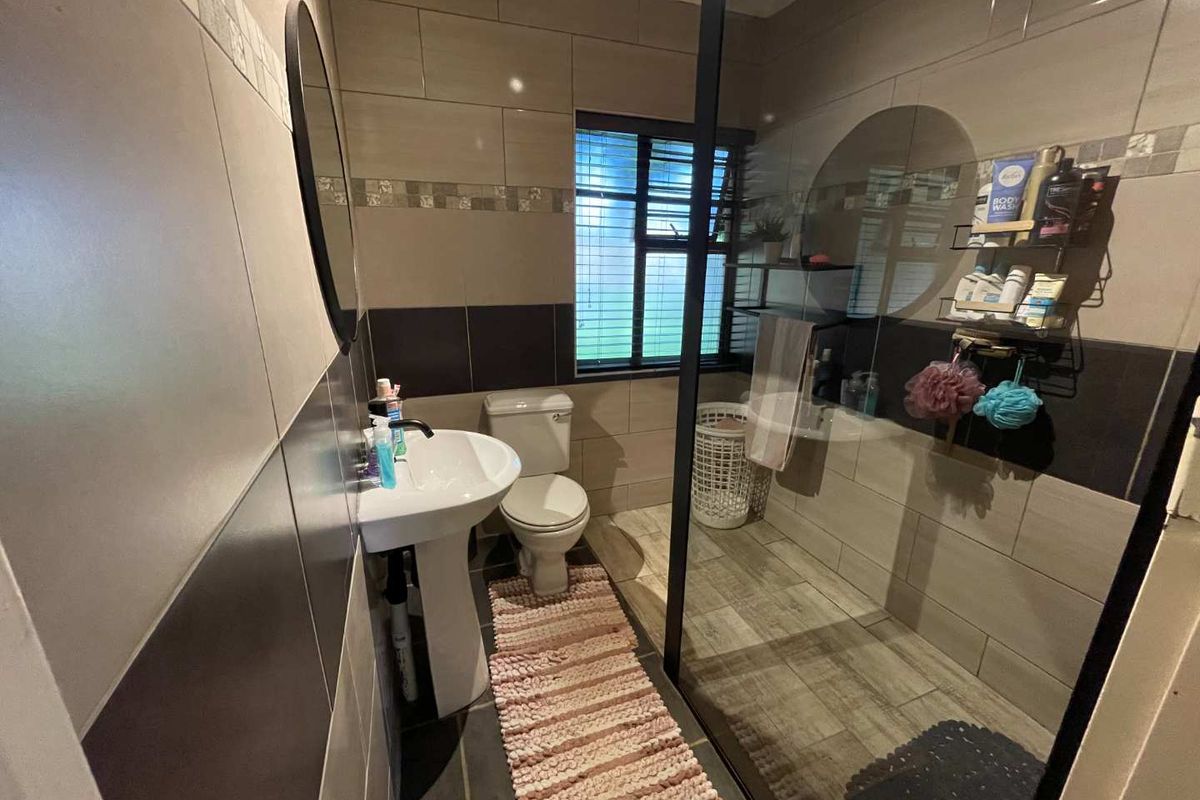 Modern bathroom featuring a walk-in shower with a black-framed glass screen, pedestal basin, toilet, and contemporary tiled finishes.