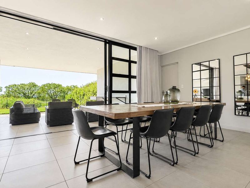 Spacious open-plan dining area featuring large format floor tiles, recessed lighting, and seamless transition to a covered patio through expansive sliding glass doors.