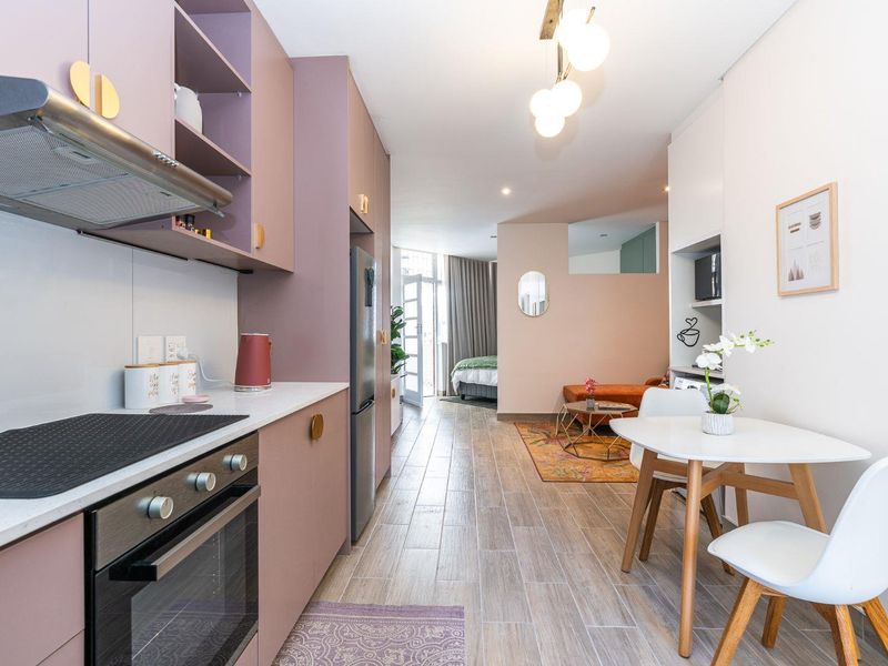 Modern open-plan apartment featuring a sleek kitchen with built-in cabinetry, stone countertops, and integrated appliances, flowing into a bright living and bedroom area.