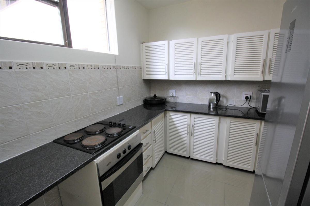 A functional kitchen featuring white louvered cabinetry, dark granite countertops, tiled splashbacks, and a built-in electric stove and oven.