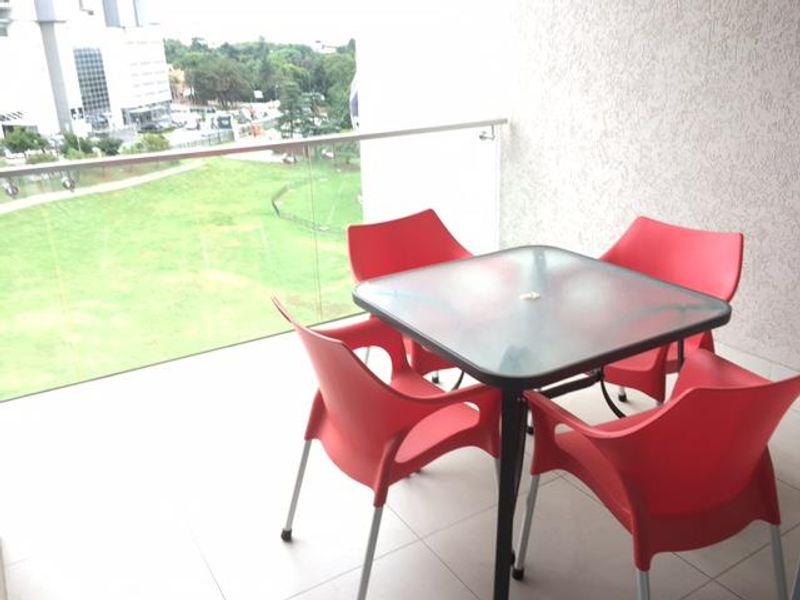 A modern balcony featuring a sleek glass balustrade and tiled flooring, offering an open view of the surrounding green space.
