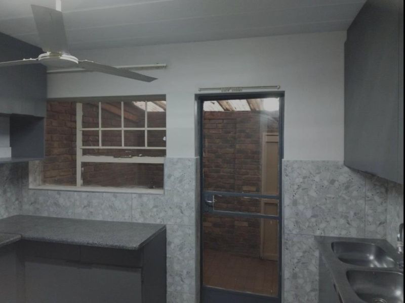 A functional kitchen area featuring built-in cabinetry, a double stainless steel sink, and a glass-paneled door leading to an enclosed outdoor space.