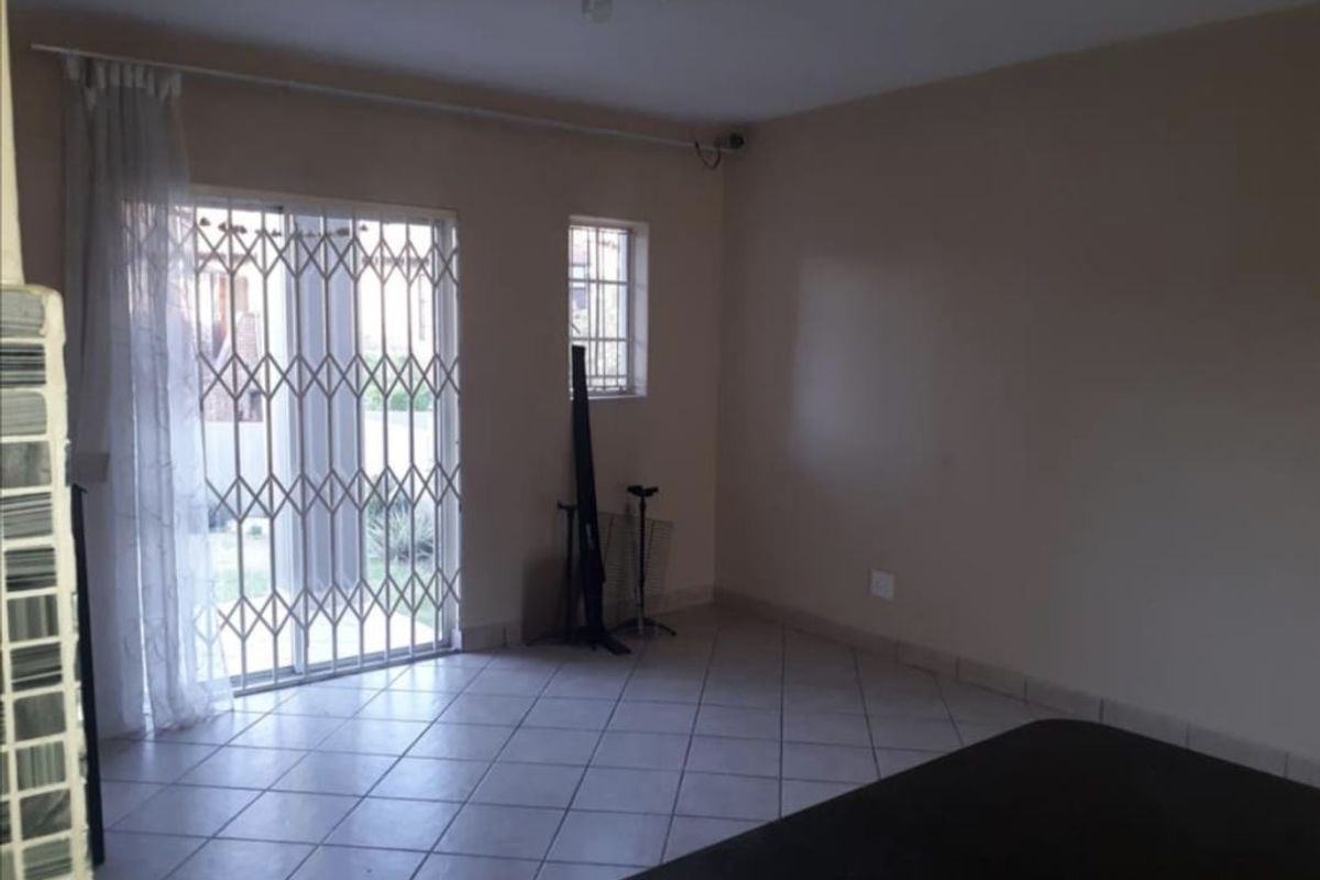 A living area featuring tiled flooring, a sliding glass door with security gate, and a small window, providing access to the exterior.