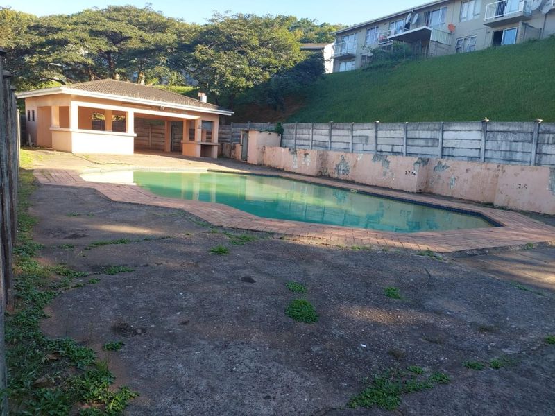 Outdoor pool area featuring a swimming pool, covered patio with built-in braai, and concrete paving, requiring maintenance and cosmetic updates.