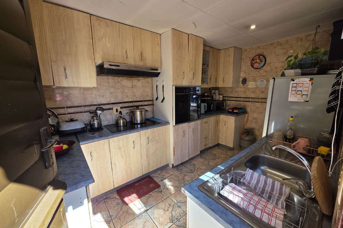 A functional kitchen featuring wood-look cabinetry, tiled splashbacks, built-in oven, extractor fan, and a double-basin stainless steel sink.