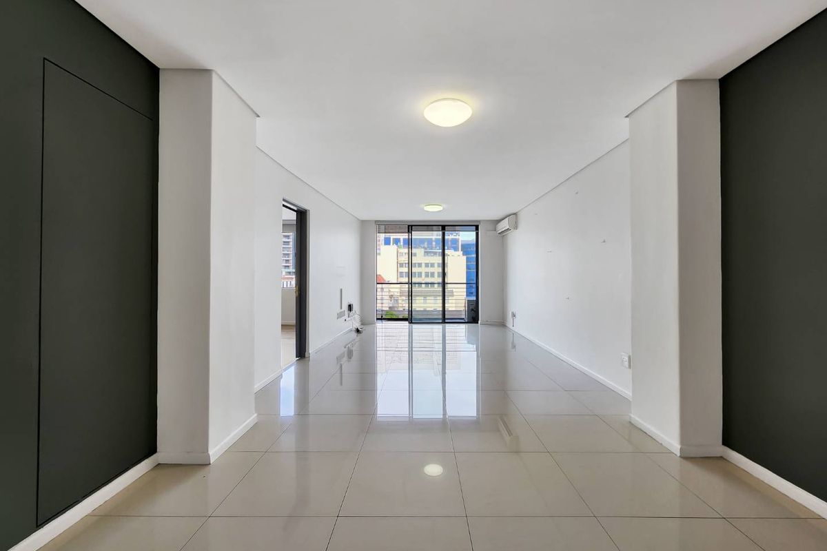 A bright, spacious, and empty living area featuring polished tile flooring, modern recessed lighting, and a sliding glass door leading to a balcony.