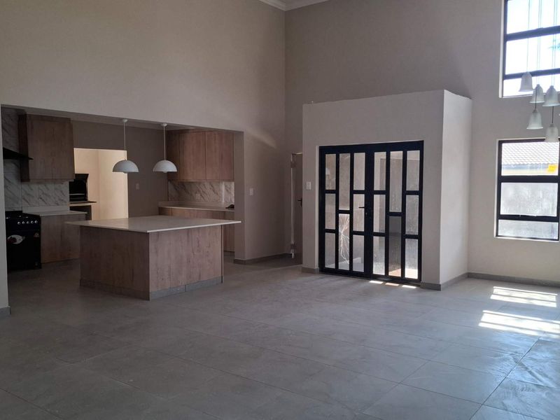 Spacious open-plan living area featuring a modern kitchen with a central island, high ceilings, and large windows providing ample natural light.