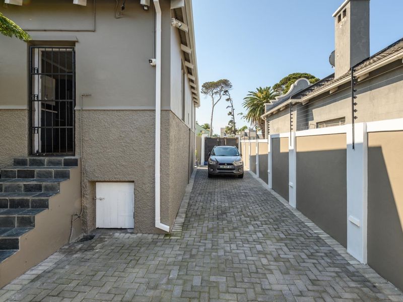 A paved side driveway leading to the rear of the property, featuring a secure boundary wall with electric fencing and tiled entrance steps.